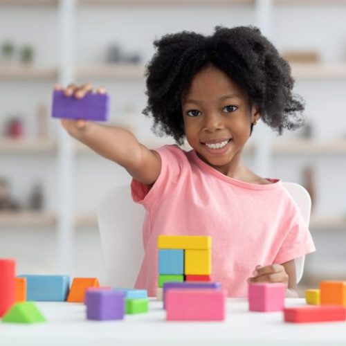 cute-little-black-girl-showing-purple-wooden-block-min-scaled-1-768x512